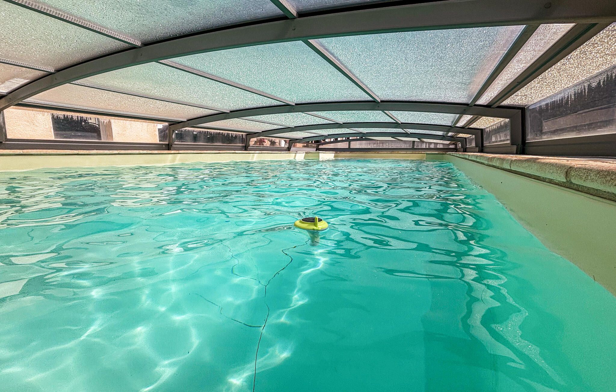 An indoor swimming pool with clear water, a diving board, and a covered roof structure.