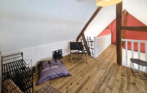A loft-style room with a sloped ceiling, a wooden floor, a black metal bench, a cushioned bench, a pillow with text, and a white railing. - Villa avec piscine privée (CharonVille)