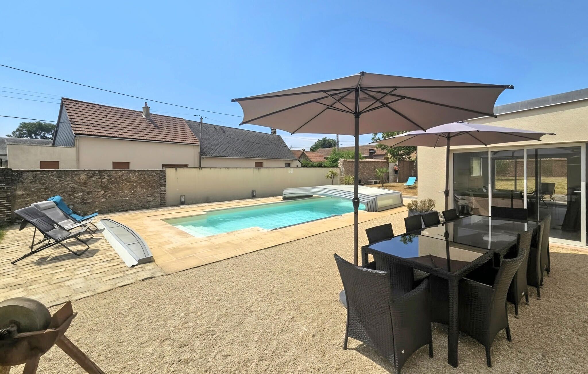 A backyard with a swimming pool, outdoor furniture, and a glass-enclosed patio area.