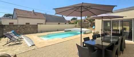 A backyard with a swimming pool, outdoor furniture, and a glass-enclosed patio area.