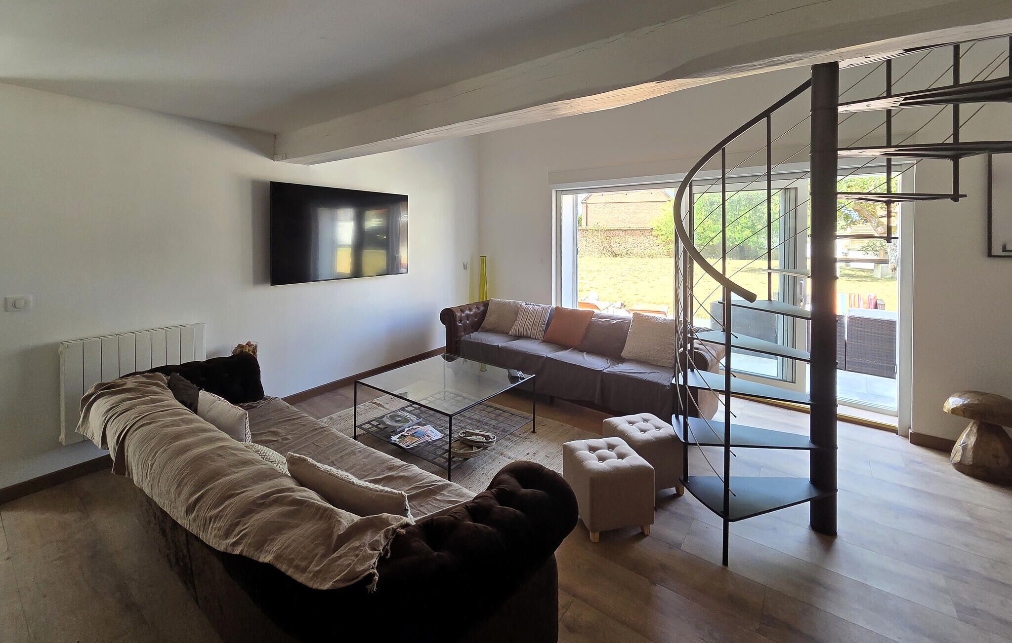 Una sala de estar moderna con sofá, otoman, mesa de centro de vidrio y una escalera en espiral.