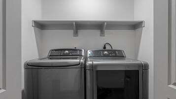 A laundry room with two front-loading washing machines and a shelf above them.