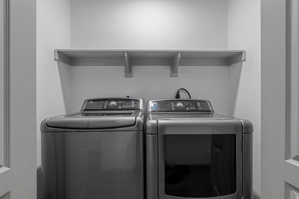 A laundry room with two front-loading washing machines and a shelf above them.