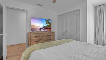 A bedroom with a bed, a wooden dresser, a television on the wall, and a ceiling fan.