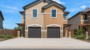 A two-story residential building with a garage, a stone foundation, and a clear blue sky.