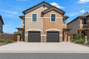 A two-story residential building with a garage, a stone foundation, and a clear blue sky.