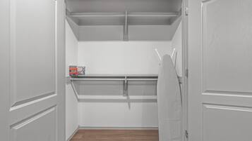 A walk-in closet with a hanging rod, a shelf, and a box of cleaning supplies.