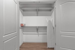 A walk-in closet with a hanging rod, a shelf, and a box of cleaning supplies.
