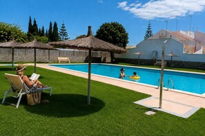 A swimming pool with a grassy area, lounge chairs, and umbrellas. - Pink Calas Blancas Apartment (Torrevieja)