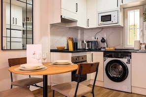 A compact kitchen with a microwave, a washing machine, and a dining area with a table and chairs. - Pink Calas Blancas Apartment (Torrevieja)