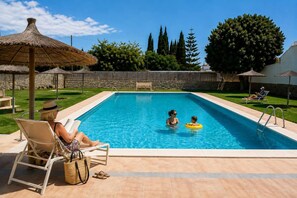 A swimming pool with lounge chairs, a person reading, and another person with a child in the water. - Pink Calas Blancas Apartment (Torrevieja)