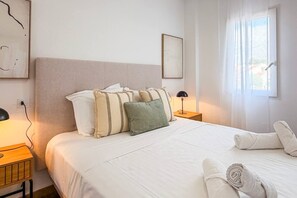 A hotel room with a bed, pillows, a bedside lamp, a window with curtains, and a towel on the bed. - Pink Calas Blancas Apartment (Torrevieja)