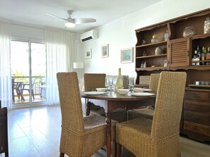 A dining area with wicker chairs, a wooden table set for four, and a ceiling fan. - Apartment Azure Oasis - Beachfront Luxury & Pools (Vilanova i la Geltru)