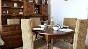 Ein Essbereich mit einem Holztisch, gedeckt für vier Personen, umgeben von gewobenen Stühlen und einer Holzkabine mit diversen Gegenständen auf den Regalen.