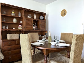 Ein Essbereich mit einem Holztisch, gedeckt für vier Personen, umgeben von gewobenen Stühlen und einer Holzkabine mit diversen Gegenständen auf den Regalen.