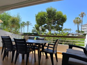 A terrace with a table and chairs, overlooking a pool and palm trees. - Apartment Azure Oasis - Beachfront Luxury & Pools (Vilanova i la Geltru)