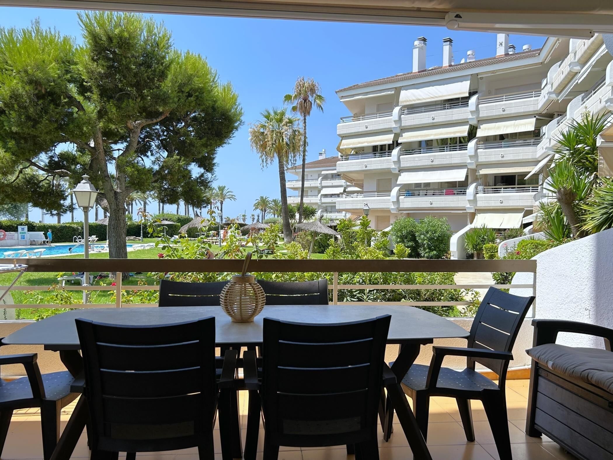 Een terras met een tafel en stoelen, met uitzicht op een zwembad en een gebouw met meerdere balkons.