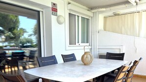 Eine Terrasse im Freien mit einem runden Tisch und Stühlen, einem Korbwägelchen und einem Fenster mit einem Schild.