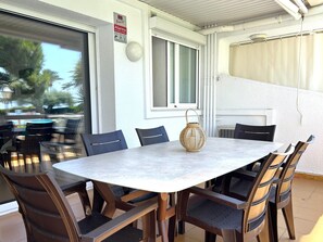 Eine Terrasse im Freien mit einem runden Tisch und Stühlen, einem Korbwägelchen und einem Fenster mit einem Schild.