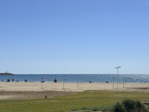 Une plage avec un ciel dégagé, un rivage sablonneux et quelques personnes. On aperçoit une petite île au loin et un phare sur la gauche.