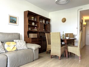 A living room with a sofa, a wooden cabinet, wicker chairs, and a dining table. - Apartment Azure Oasis - Beachfront Luxury & Pools (Vilanova i la Geltru)