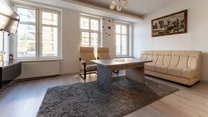 Ett rymligt vardagsrum med ett stort fönster, en soffa, ett matbord och en kristallkrona.