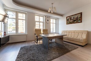 Ein geräumiges Wohnzimmer mit großem Fenster, einer Couch, einem Esstisch und einer Kristallleuchtre.