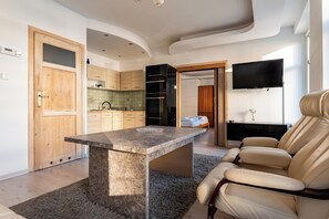 Ein modernes Wohnzimmer mit einem Stehtisch, einem beigefarbenen Ledersofa und einem an der Wand befestigten Flachbildfernseher.
