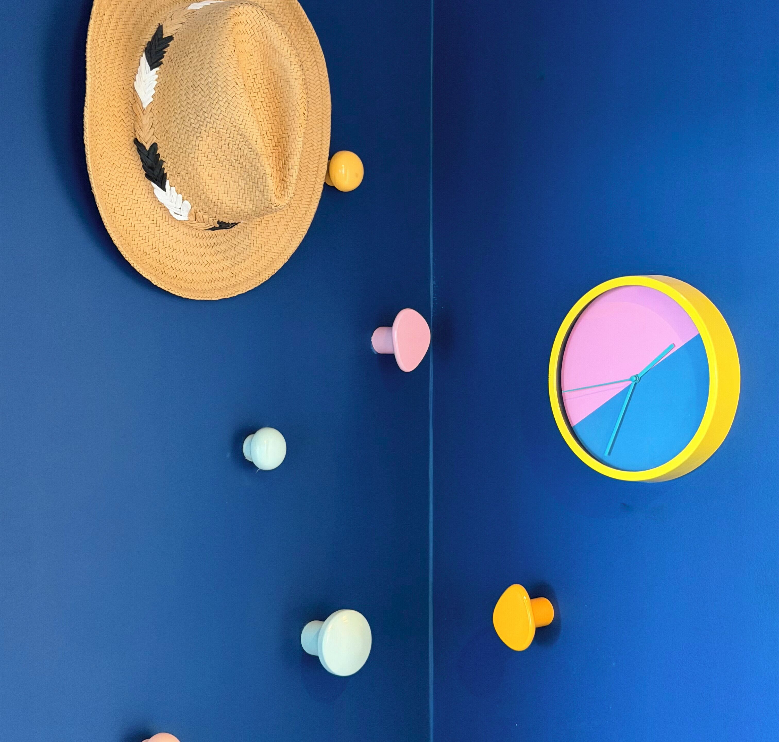 A room with a blue wall, a straw hat, a clock, and several small round objects.