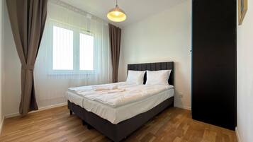 Un dormitorio con cama, cortinas, una ventana y una lámpara colgante.