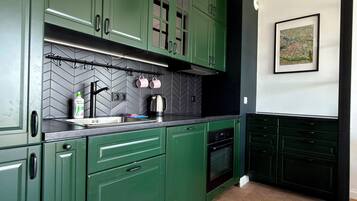 Cocina con gabinetes verdes, salpicadero negro y patrón de baldosas en espiga.