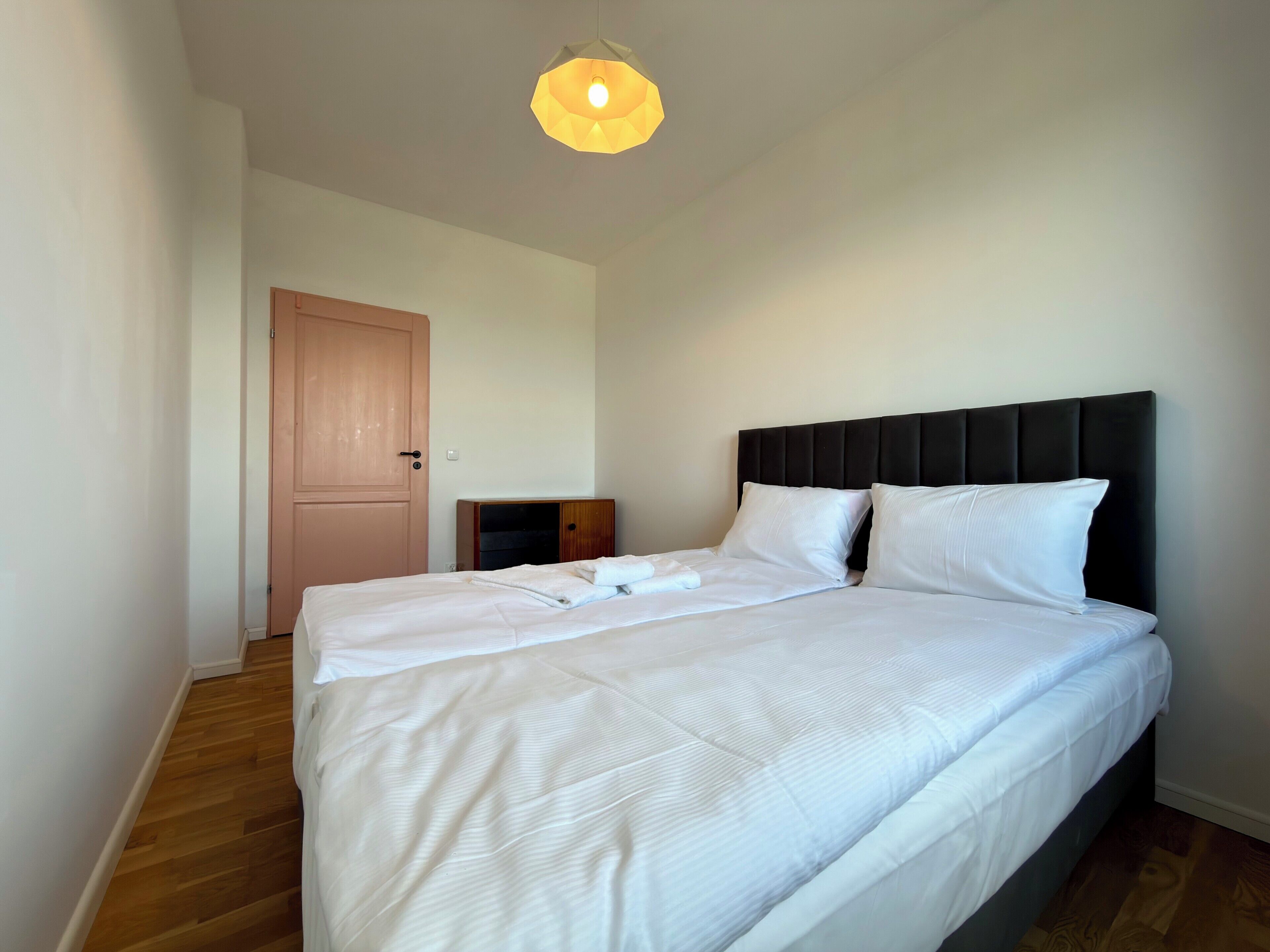 A bedroom with a bed, a wooden door, and a light fixture.