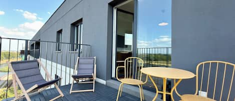 A balcony with a black tiled floor, two lounge chairs, a small table, and a chair.