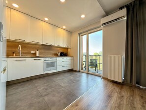A modern kitchen with a built-in oven, a coffee maker, and a large window leading to a balcony.