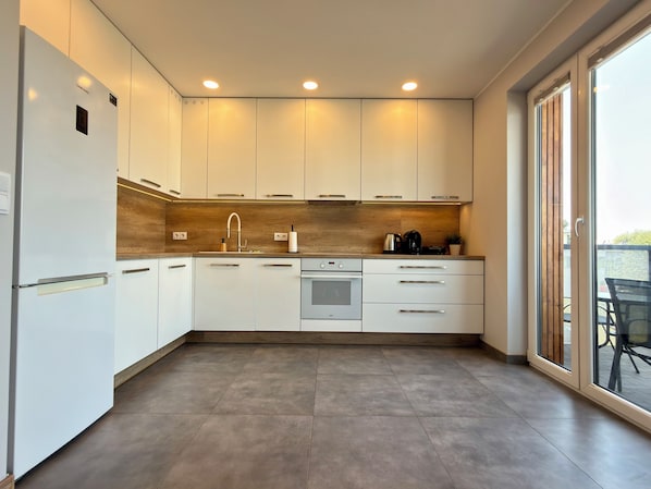 A modern kitchen with white cabinets, a stainless steel refrigerator, a built-in oven, and a coffee maker.