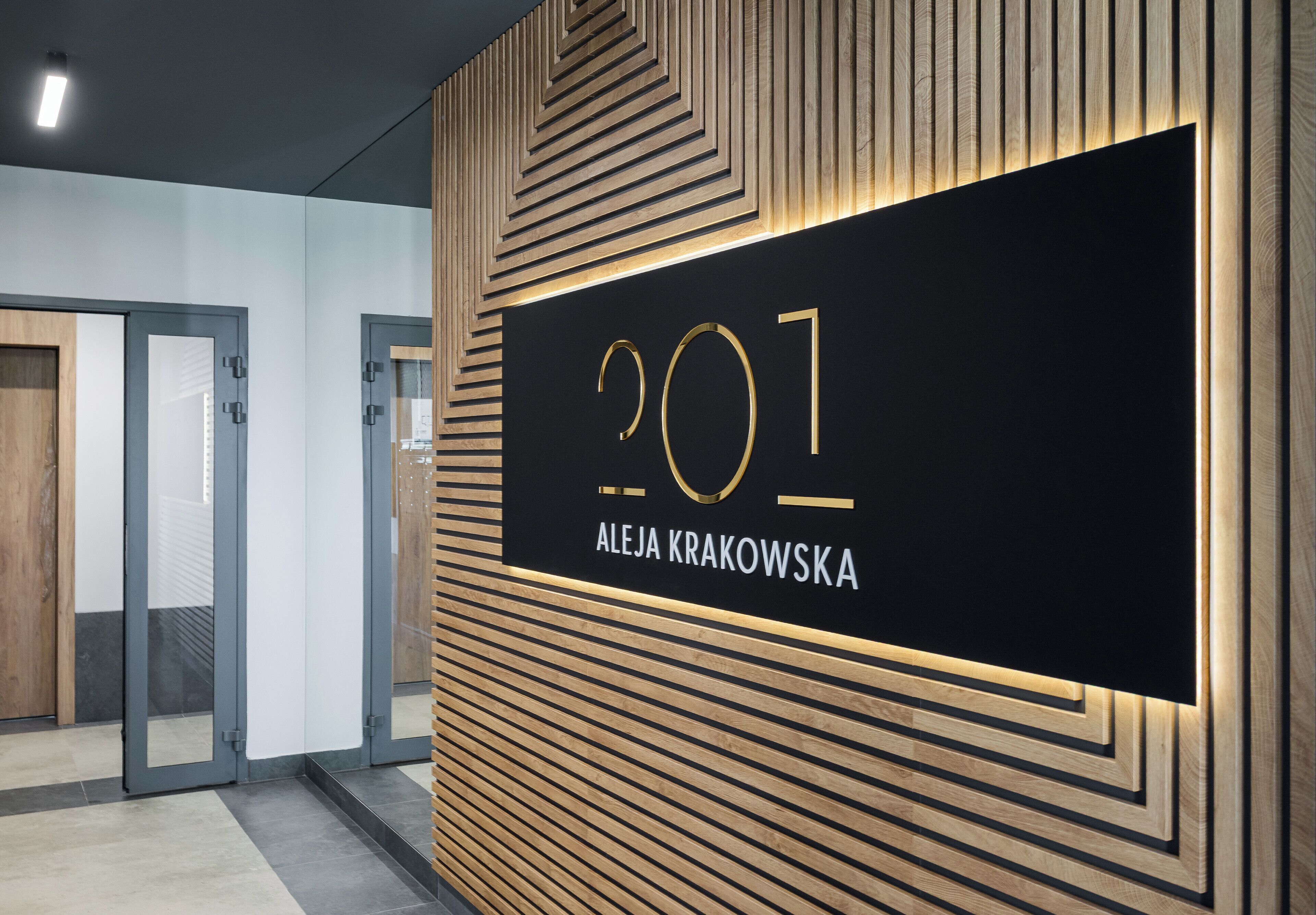 A modern interior with a black wall displaying the number '201' and the name 'Aleja Krakowska'.