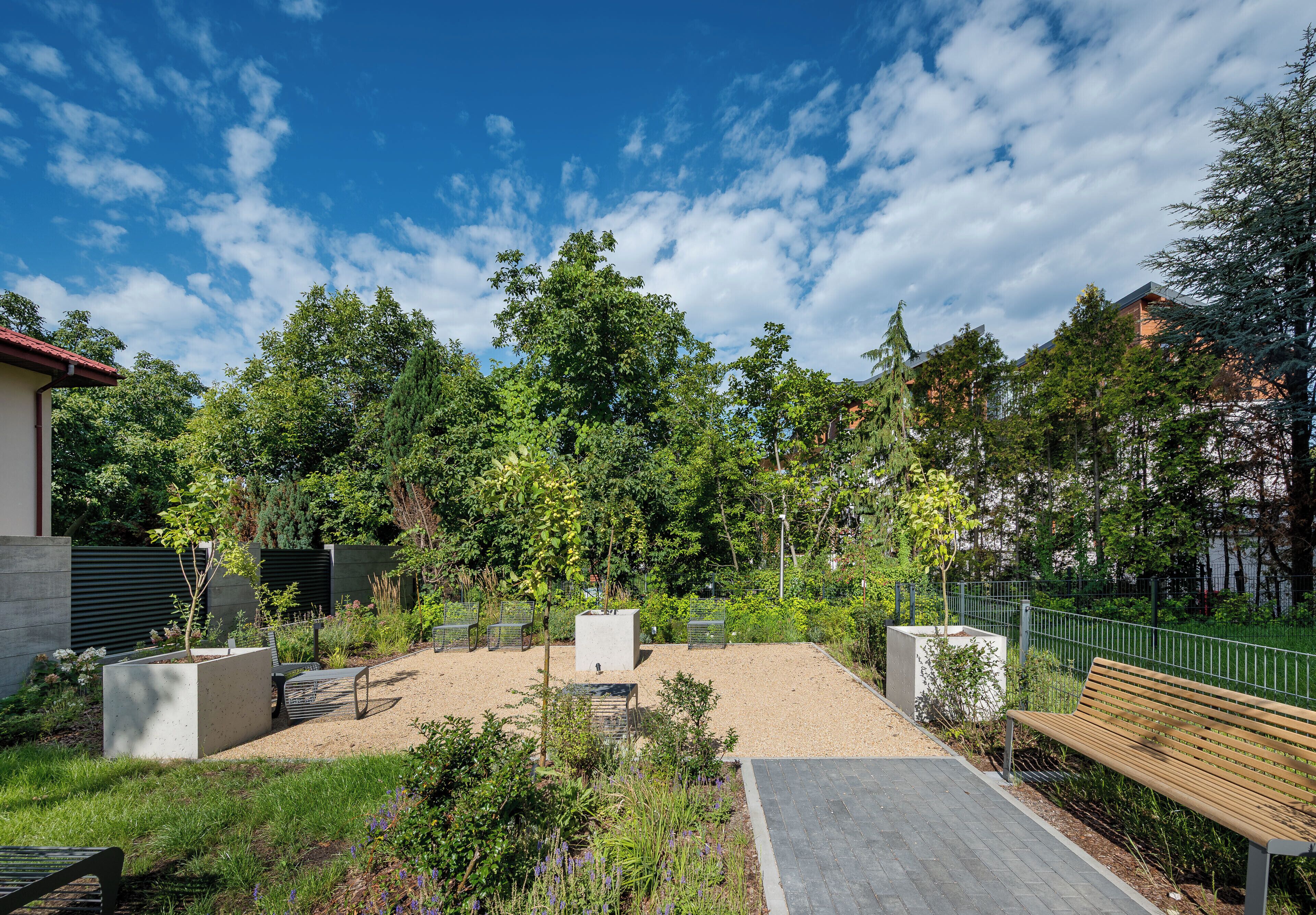 An outdoor garden area with benches, a gravel path, and a variety of trees and shrubs.