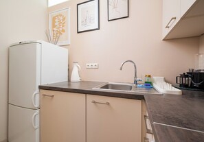 A kitchenette with a white refrigerator, a sink with a faucet, and a kettle on the counter. - Krucza City Heart Apartment (Warszawa)