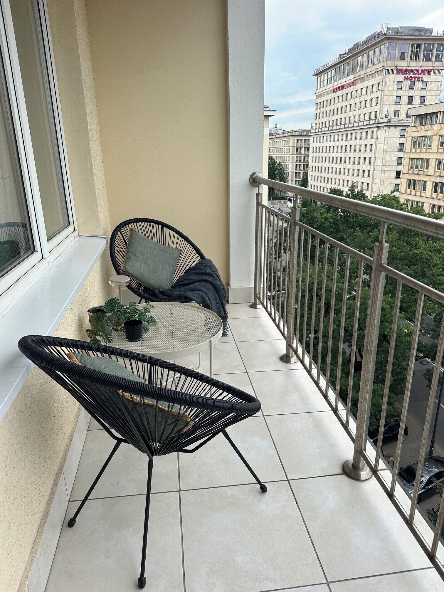 A balcony with two black chairs, a small table, and a potted plant.