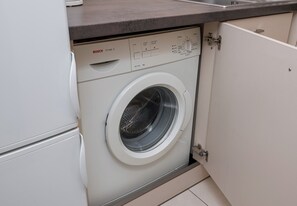 Lavadora Bosch Maxx 4 blanca y compacta, con panel de control, ubicada en una cocina con encimera gris.
