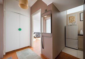 Un intérieur moderne avec une armoire blanche, un miroir, un objet circulaire vert accroché au mur, un canapé gris et un coin cuisine avec un réfrigérateur.