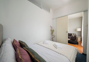 Habitación de hotel con cama, almohadas, mesita de noche, espejo y vista al área de estar.