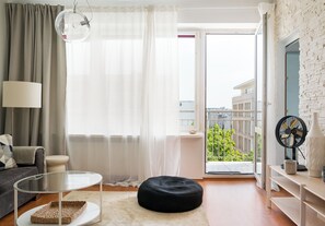Un salon moderne avec une table en verre, un pouf noir et une vue sur la ville, visible à travers une grande fenêtre.