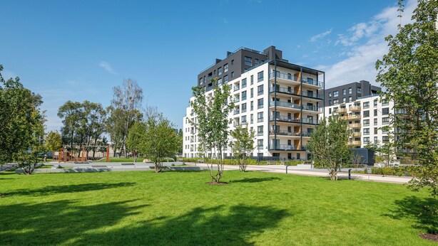 Un immeuble d’appartements moderne, doté de nombreux balcons, entouré d’un espace verdoyant bien entretenu et d’arbres.