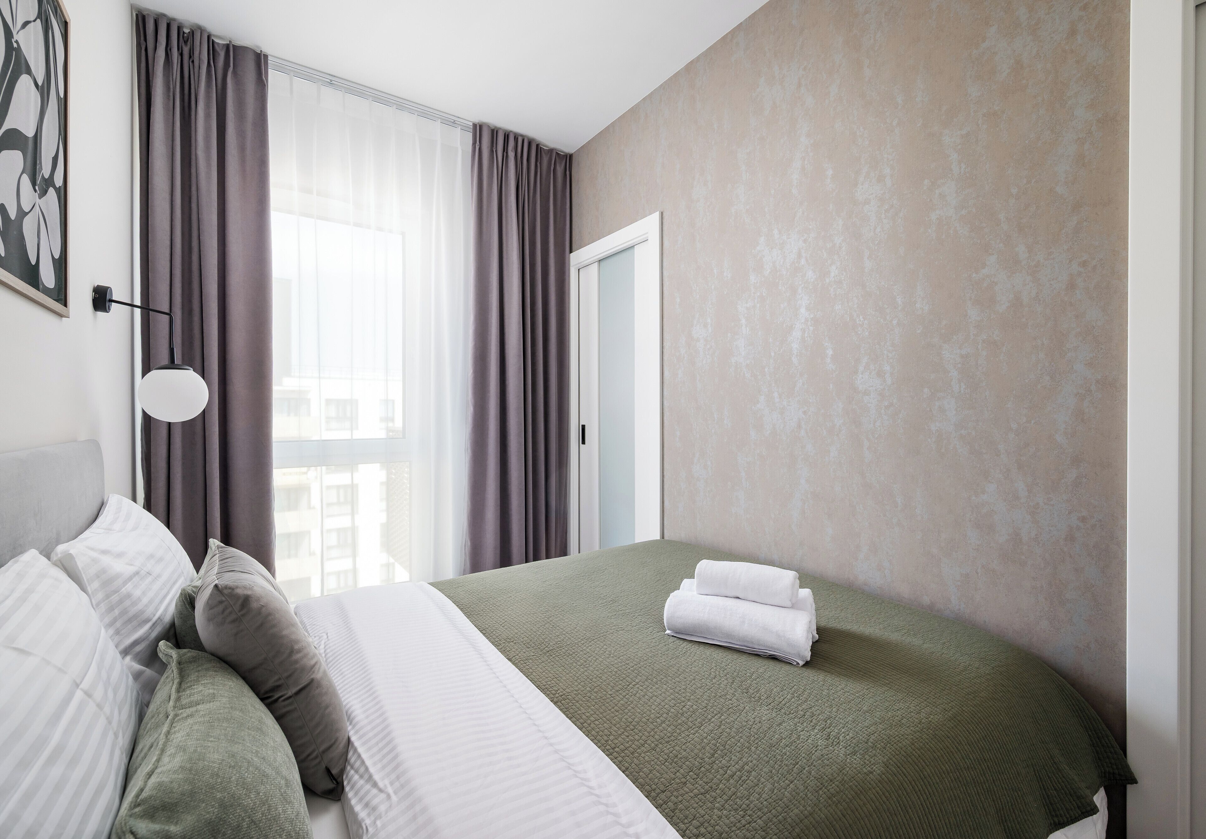 A hotel room with a bed, a window with curtains, a door, and a wall with a textured finish.
