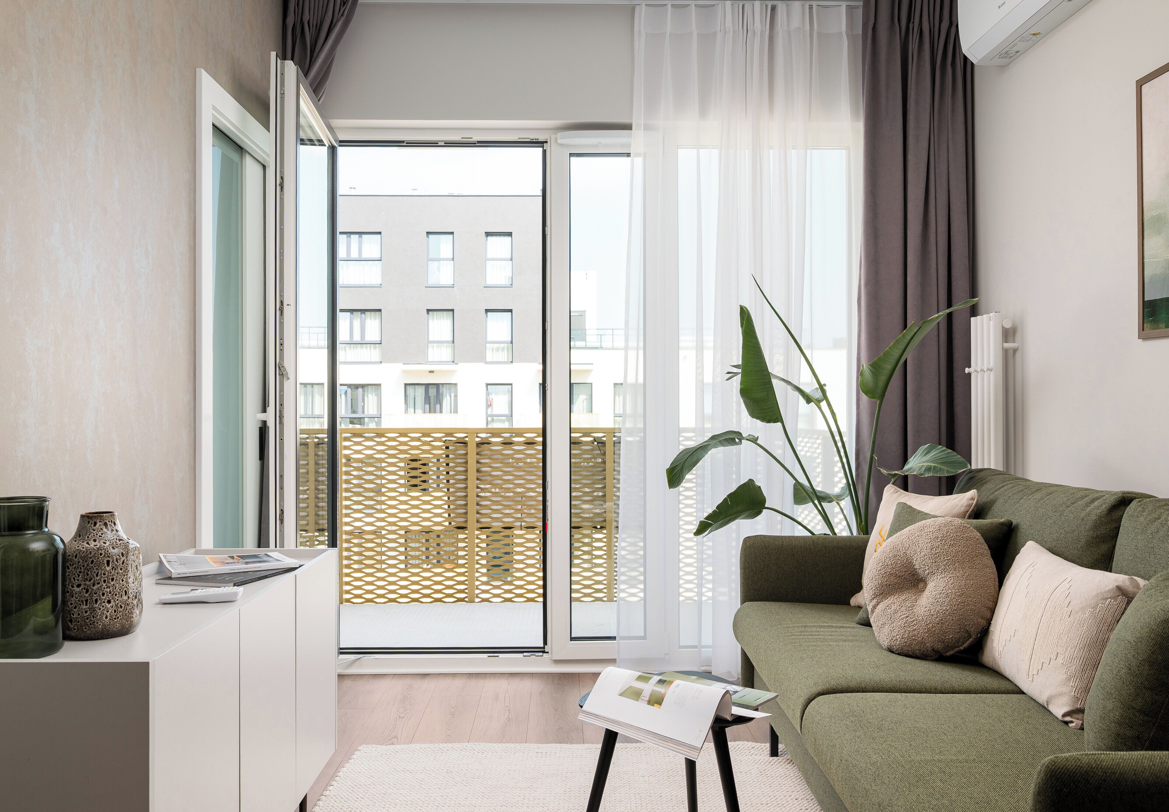 Ein modernes Wohnzimmer mit einer Couch, einem Couchtisch, einer Zimmerpflanze und Blick auf ein Gebäude durch eine Glastür.