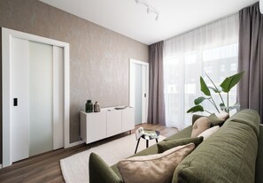 A modern living room with a sofa, a white console table, and a large window with curtains. - Wola Redutowa Superior Apartment (Warszawa)