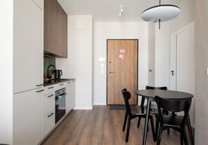 Une cuisine moderne avec des armoires blanches, un comptoir noir et un four encastré. On y trouve également un coin repas avec une table et des chaises noires.