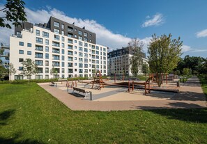 A modern apartment building with multiple floors, balconies, and a well-maintained park area with playground equipment. - Wola Redutowa Superior Apartment (Warszawa)