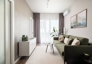 A modern living room with a green sofa, a white cabinet, and a large window with curtains. - Wola Redutowa Superior Apartment (Warszawa)